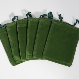 May include: Seven green velvet drawstring pouches with dark green drawstrings. The pouches are arranged in a fan shape.