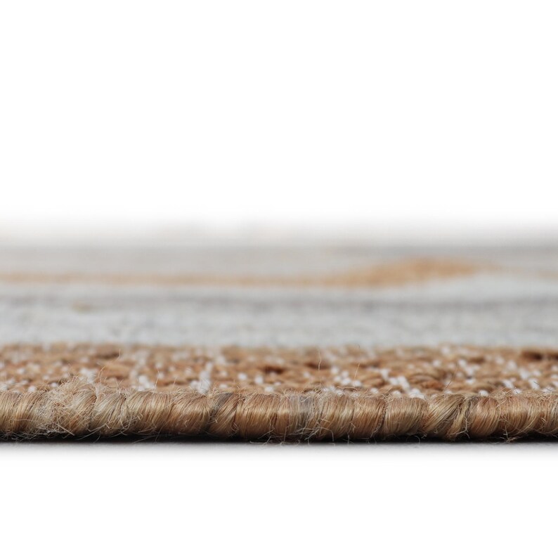 Peut inclure: Gros plan sur un tapis beige et marron. Le tapis a une surface textur&eacute;e avec un motif tiss&eacute;. Le bord du tapis est visible, montrant l'&eacute;paisseur et la construction du mat&eacute;riau. La palette de couleurs est neutre, avec des nuances de beige et de marron.