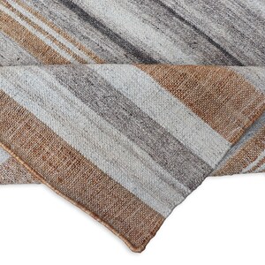 Peut inclure: Un tapis enroul&eacute; avec un motif &agrave; rayures diagonales. Le tapis pr&eacute;sente des rayures altern&eacute;es marron, grises et blanc cass&eacute;. Les bords du tapis sont visibles, montrant la texture tiss&eacute;e et les variations de couleurs.