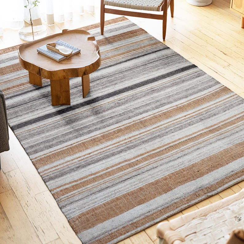 Peut inclure: Un tapis rectangulaire &agrave; rayures horizontales dans des tons de gris, de marron et de blanc cass&eacute;. Un motif ray&eacute; orne le tapis. Un tapis de sol est pos&eacute; sur un plancher en bois. Le tapis ajoute de la chaleur et de la texture &agrave; la pi&egrave;ce.