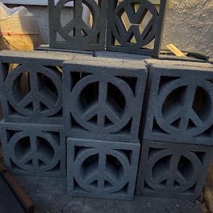 Puede incluir: Un conjunto de bloques de hormigón gris, algunos con el símbolo de la paz y otros con el logotipo de Volkswagen. Los bloques cuadrados tienen diseños recortados, adecuados para fines decorativos o de construcción.