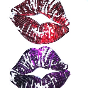 May include: Two embroidered patches shaped like lips, one in red and white sequins and the other in purple and white sequins. Each patch features a striped pattern of colored sequins alternating with white sequins to form the shape of open lips.