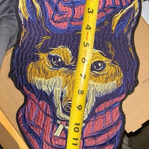 May include: Embroidered patch featuring a wolf's head design. The patch is primarily purple, with gold, red, and blue accents. The patch measures approximately 12 inches in height.