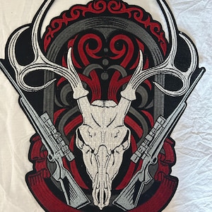 Op de afbeelding: Geborduurde patch met een herten schedel met geweien, geflankeerd door twee geweren. Het ontwerp gebruikt rood, zwart, grijs en wit, met sierlijke krullen en een rode banner aan de onderkant. Voor jassen of tassen.