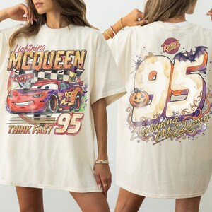 May include: An off-white t-shirt featuring a graphic of Lightning McQueen from Cars on the front with the text Lightning McQueen, Cars, and Think Fast 95. The back displays a large 95 with a pumpkin, a bat, and the text Lightning McQueen.