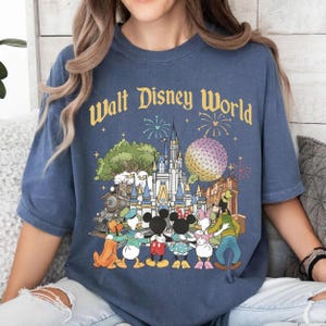 May include: Blue t-shirt with "Walt Disney World" text and a colorful graphic featuring Disney characters, a castle, Spaceship Earth, and fireworks. The design includes Mickey Mouse, Minnie Mouse, Donald Duck, Goofy, and Pluto.