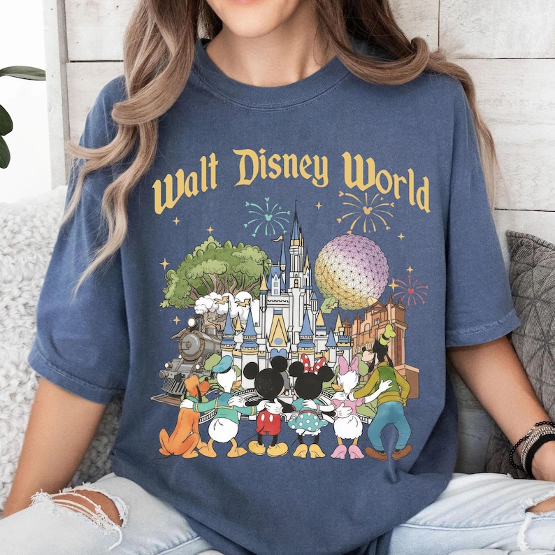 May include: Blue t-shirt with "Walt Disney World" text and a colorful graphic featuring Disney characters, a castle, Spaceship Earth, and fireworks. The design includes Mickey Mouse, Minnie Mouse, Donald Duck, Goofy, and Pluto.