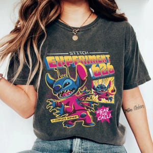 Puede incluir: Camiseta gris oscuro con un gr&aacute;fico colorido de Stitch de Lilo & Stitch. El dise&ntilde;o incluye el texto "STITCH EXPERIMENT 626", "A COMPLETE MAYHEM!" y "HEAR THE CALL!". Una camiseta divertida para los fans de la pel&iacute;cula animada.