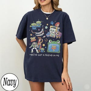 Puede incluir: Una camiseta azul marino de manga corta con un estampado gr&aacute;fico colorido de personajes de Toy Story, incluyendo a Woody, Buzz Lightyear y alien&iacute;genas. El dise&ntilde;o incluye el texto Disney Pixar, Toy Story, Toy Story 5 y You've Got A Friend In Me.