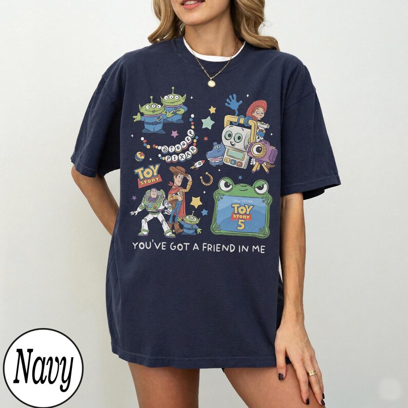 Puede incluir: Una camiseta azul marino de manga corta con un estampado gr&aacute;fico colorido de personajes de Toy Story, incluyendo a Woody, Buzz Lightyear y alien&iacute;genas. El dise&ntilde;o incluye el texto Disney Pixar, Toy Story, Toy Story 5 y You've Got A Friend In Me.