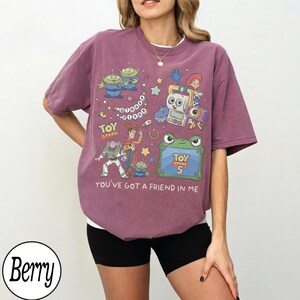 Puede incluir: Una camiseta de manga corta color baya con un estampado gr&aacute;fico de personajes de Toy Story, incluyendo a Woody, Buzz Lightyear y alien&iacute;genas. El dise&ntilde;o incluye el texto "Toy Story", "Toy Story 5" y "You've Got A Friend In Me" con estrellas.