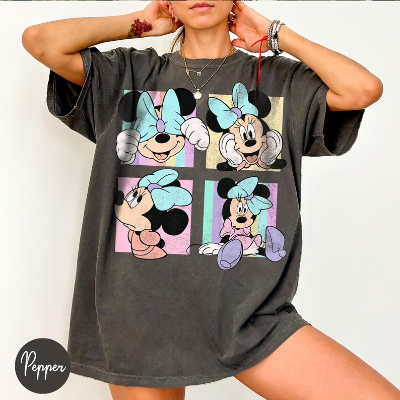 May include: Dark grey oversized t-shirt with a four-panel graphic of Minnie Mouse in different poses. Each panel has a pastel background with Minnie Mouse wearing a light blue bow and a pink dress. The shirt has a vintage, worn appearance.