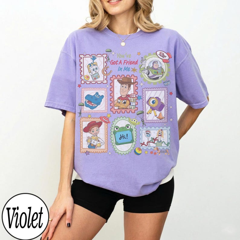May include: A light violet short-sleeve t-shirt featuring a graphic print of various Toy Story characters in postage stamp-style frames. The text "You've Got A Friend In Me" is printed in the center, along with a small green frog holding a sign saying "Hi!"
