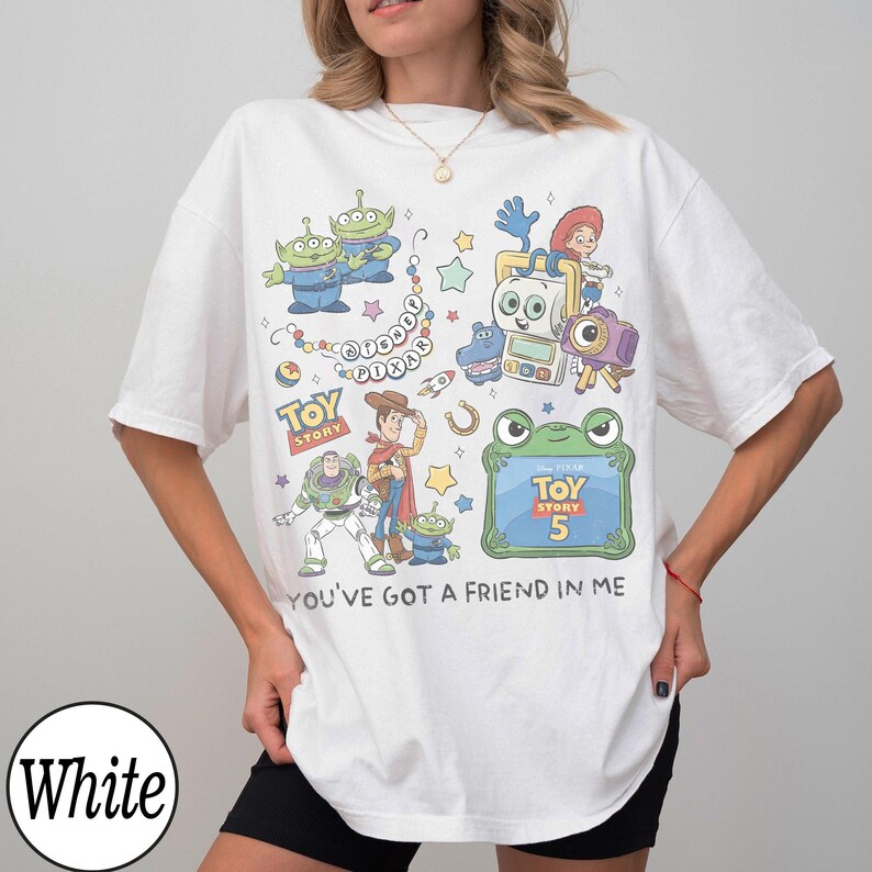 Puede incluir: Una camiseta blanca con un estampado gr&aacute;fico colorido de personajes de Toy Story, incluyendo a Woody, Buzz Lightyear y los Aliens. El dise&ntilde;o incluye el texto Disney Pixar, Toy Story 5 y la frase You've Got A Friend In Me.