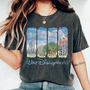 May include: A charcoal gray t-shirt featuring a graphic print of four vertical panels displaying Walt Disney World landmarks, including a castle, a geodesic dome, a large tree, and a tower, with the text Walt Disney World printed below.