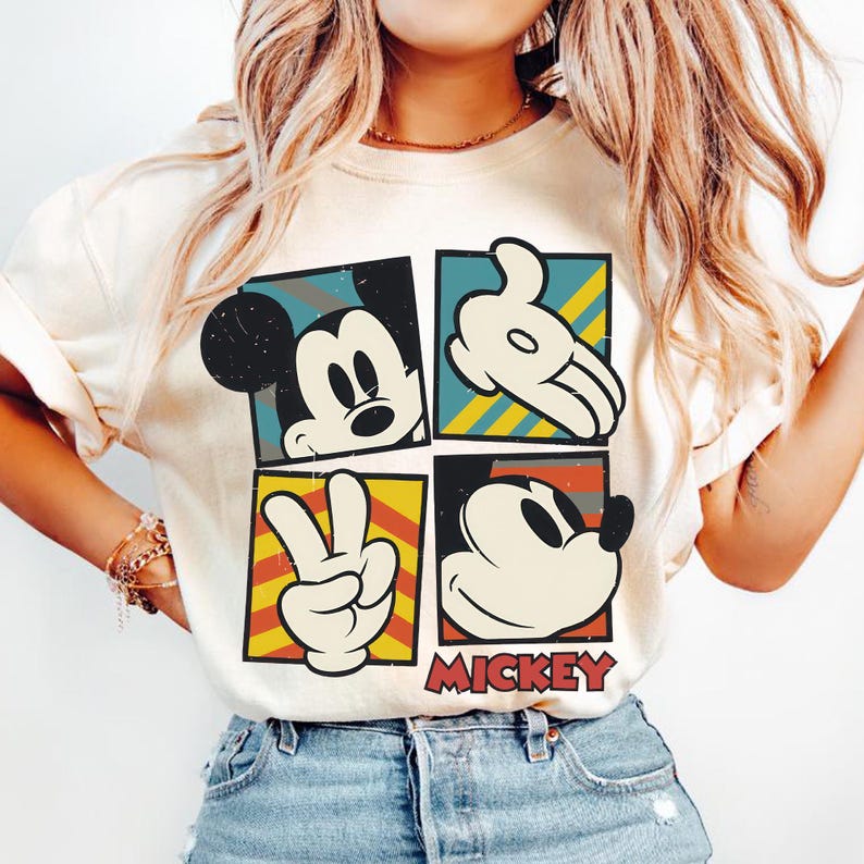 Puede incluir: Camiseta color crema con un dise&ntilde;o de cuatro paneles con im&aacute;genes de Mickey Mouse. Cada panel muestra una pose diferente: un primer plano de su rostro, una mano enguantada, un signo de la paz y otra vista de la cara. La palabra "MICKEY" est&aacute; impresa en rojo.