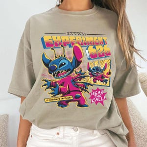 Puede incluir: Camiseta marr&oacute;n claro con un gr&aacute;fico colorido de Stitch de Lilo & Stitch. El dise&ntilde;o incluye el texto "Stitch Experiment 626", "A Complete Mayhem!" y "Hear the Call!" en estilo c&oacute;mic.
