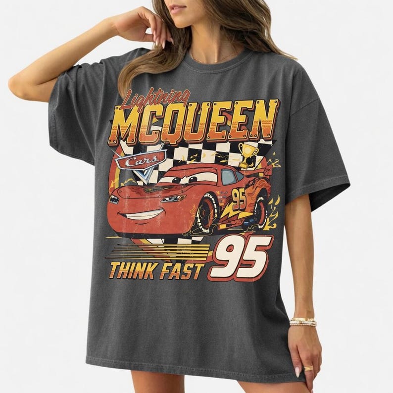 May include: Dark gray Lightning McQueen Cars graphic t-shirt. The design features a red race car with the number 95, a checkered flag, and the text "Lightning McQueen" and "Think Fast".