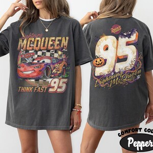 May include: A charcoal gray t-shirt featuring a graphic of Lightning McQueen from Cars on the front with the text Lightning McQueen, Cars, and Think Fast 95. The back displays a large 95 with a pumpkin, a bat, and the text Lightning McQueen.