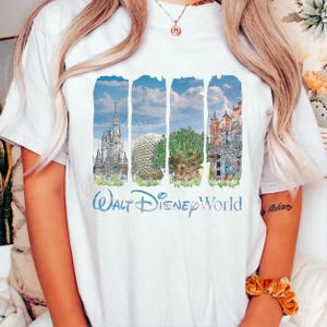 May include: A white t-shirt featuring a graphic print of four vertical panels displaying Walt Disney World landmarks, including Cinderella Castle, Spaceship Earth, the Tree of Life, and the Hollywood Tower Hotel, with the text Walt Disney World below.