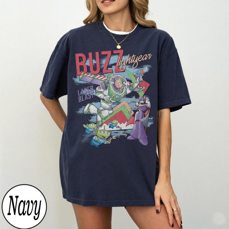 May include: Navy blue t-shirt featuring a graphic of Buzz Lightyear, aliens, and Zurg with the text "BUZZ lightyear" and "LASER BLAST". The design is in shades of green, red, purple, and white.