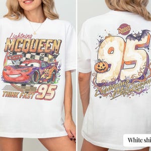 May include: A white t-shirt featuring a graphic of Lightning McQueen from the movie Cars on the front with the text Lightning McQueen and Think Fast 95. The back displays a large number 95 with a pumpkin, a bat, and the text Lightning McQueen.