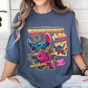 Puede incluir: Camiseta azul con un gr&aacute;fico colorido de Stitch de Lilo & Stitch. El dise&ntilde;o incluye el texto "Stitch Experiment 626", "A Complete Mayhem!" y "Hear the Call!" en estilo c&oacute;mic.