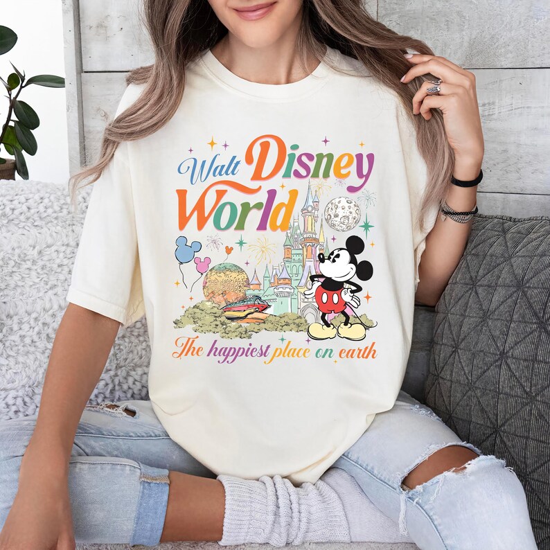 以下が含まれることがあります： ウォルト・ディズニー・ワールドのカラフルなグラフィックが特徴のクリーム色のTシャツ。デザインにはミッキーマウス、お城、風船、そして「The happiest place on earth」というフレーズが含まれています。