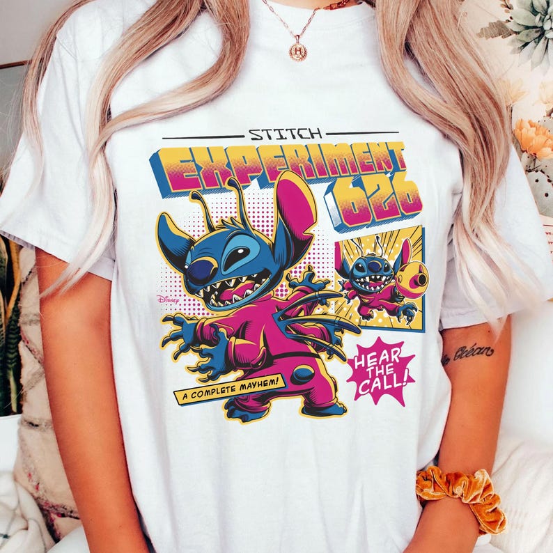 Puede incluir: Camiseta blanca con un gr&aacute;fico colorido de Stitch, etiquetado como "Experiment 626". El dise&ntilde;o incluye a Stitch con un mono rosa con detalles azules, y los textos "A Complete Mayhem!" y "Hear the Call!"