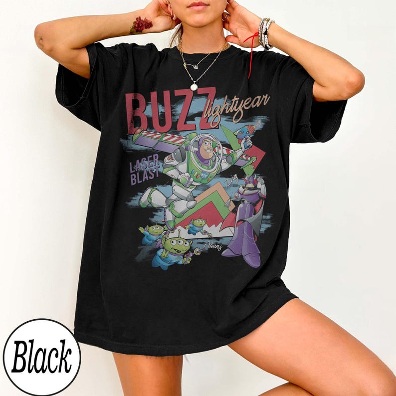 May include: Black t-shirt featuring a graphic of Buzz Lightyear from Toy Story. The design includes the text "BUZZ lightyear" and "LASER BLAST", along with images of Buzz, aliens, and Zurg. The shirt is a relaxed fit.