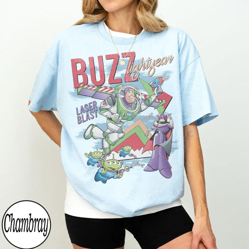 May include: Light blue t-shirt featuring a graphic of Buzz Lightyear from Toy Story. The design includes the words "BUZZ lightyear" and "LASER BLAST" in red and white. The shirt has a vintage, cartoon-like aesthetic.