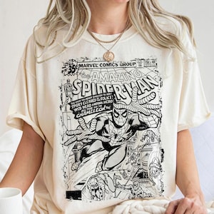 Pu&ograve; includere: Una t-shirt color crema con una stampa grafica in bianco e nero di una copertina di un fumetto vintage Marvel Comics The Amazing Spider-Man. Il design include il titolo, i dettagli del numero e illustrazioni di Spider-Man in pose d'azione.