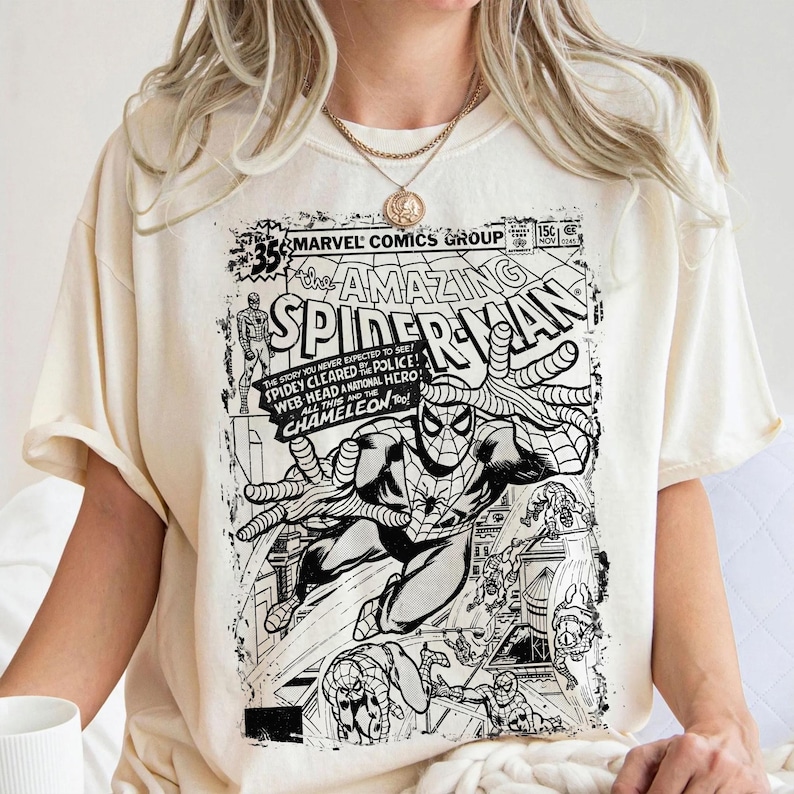 Pu&ograve; includere: Una t-shirt color crema con una stampa grafica in bianco e nero di una copertina di un fumetto vintage Marvel Comics The Amazing Spider-Man. Il design include il titolo, i dettagli del numero e illustrazioni di Spider-Man in pose d'azione.