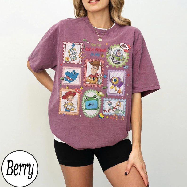 May include: A berry-colored short-sleeve t-shirt featuring a graphic print of various Toy Story characters arranged in postage stamp-style frames. The text "You've Got A Friend In Me" is printed in the center above an illustration of Woody.