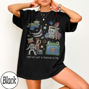 Puede incluir: Una camiseta negra de manga corta con un estampado gr&aacute;fico colorido de varios personajes de Toy Story, incluyendo a Woody, Buzz Lightyear y alien&iacute;genas. El dise&ntilde;o incluye el texto Disney Pixar, Toy Story, Toy Story 5 y You've Got A Friend In Me.