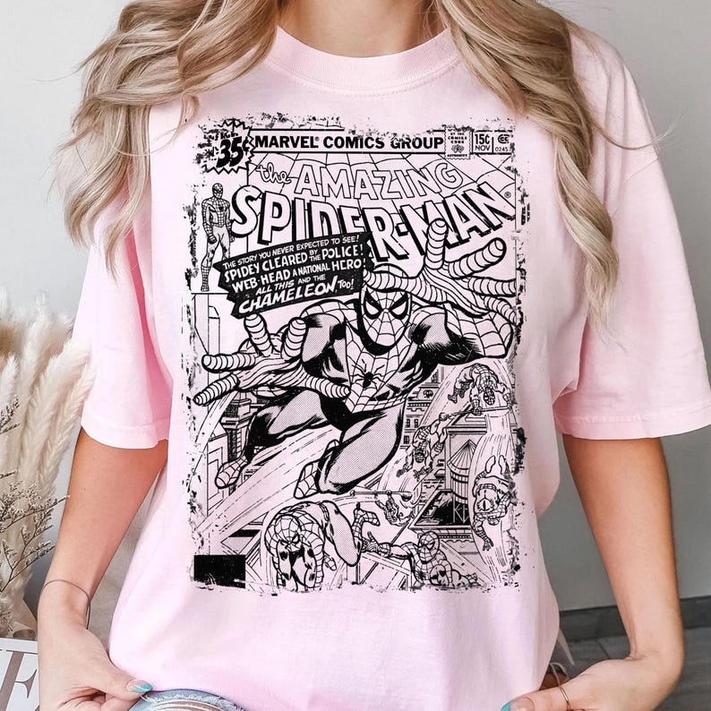 Pu&ograve; includere: Una t-shirt a maniche corte rosa chiaro con una stampa grafica in bianco e nero della copertina di un fumetto vintage Marvel Comics The Amazing Spider-Man. Il design include il titolo, il numero dell'albo e illustrazioni di Spider-Man.