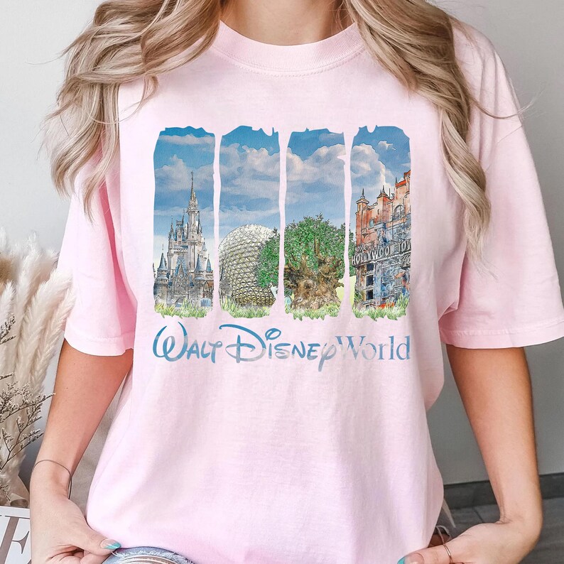 May include: A light pink short-sleeve t-shirt featuring a graphic print of four vertical panels depicting iconic theme park landmarks, including a castle, a geodesic dome, a large tree, and a tower, with the text Walt Disney World below.