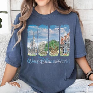 May include: A blue short-sleeve t-shirt featuring a graphic print of four vertical panels displaying iconic Walt Disney World landmarks, including a castle, a geodesic dome, a large tree, and a tower, with the text Walt Disney World below.