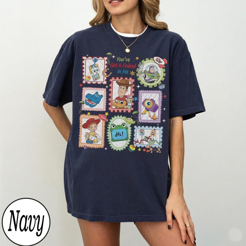 May include: A navy blue short-sleeve t-shirt featuring a graphic print of various cartoon characters from the Toy Story franchise arranged in postage stamp-style frames, with the text "You've Got A Friend In Me" and "Hi!" printed on the front.