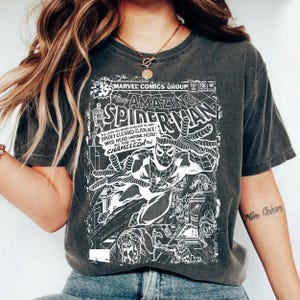 Pu&ograve; includere: Una t-shirt grigio antracite con una stampa grafica bianca di una copertina di un fumetto vintage Marvel Comics The Amazing Spider-Man. Il design include il titolo, i dettagli del numero e un'illustrazione di Spider-Man in una posa dinamica.