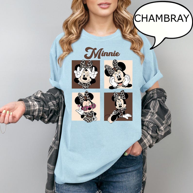 May include: Light blue t-shirt featuring a Minnie Mouse graphic. The graphic includes four panels with different poses of Minnie Mouse wearing a leopard print bow and dress. The word "Minnie" is printed above the panels in a brown script font.