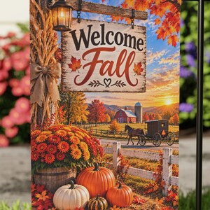 May include: A rectangular garden flag hanging on a black metal stand, featuring a printed scene of a wooden sign that reads Welcome Fall, orange pumpkins, a lantern, a horse-drawn carriage, and autumn foliage against a sunset sky.