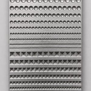 Könnte beinhalten: Eine rechteckige, silberfarbene Metallplatte mit einer strukturierten Oberfläche, die im oberen Bereich Reihen von geprägten kreisförmigen Vertiefungen und im unteren Bereich Reihen von geprägten pyramidenförmigen geometrischen Mustern aufweist, mit gebürsteter Oberfläche.