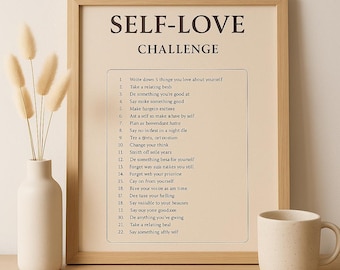 May include: A framed print with the text "SELF-LOVE CHALLENGE" and a list of 22 prompts. A white ceramic mug and a vase with dried flowers are on a wooden surface.