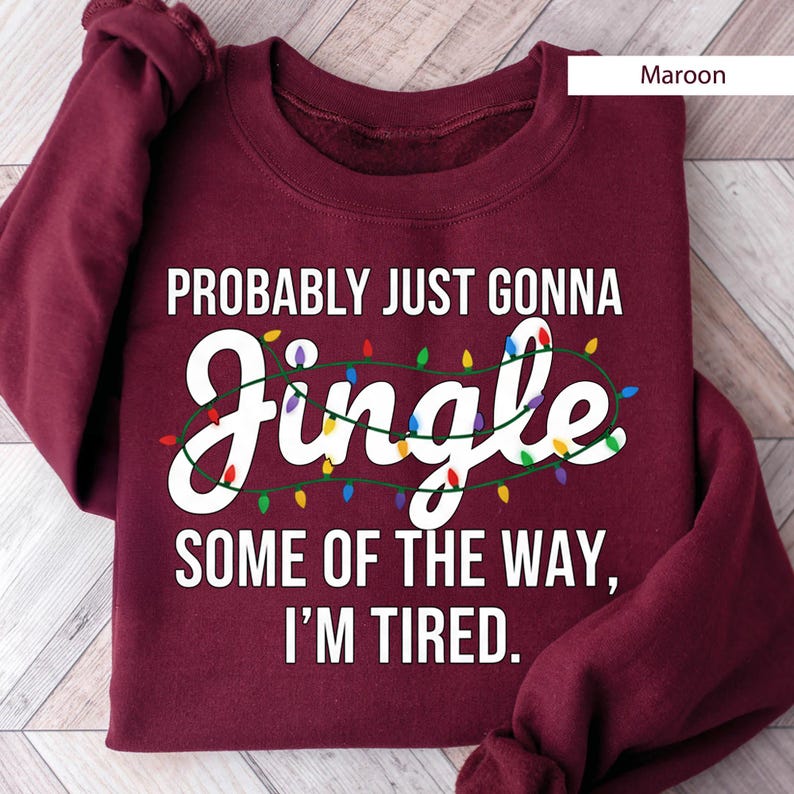 A maroon sweatshirt with a humorous text printed on it, which reads "Probably Just Gonna Jingle Some of the Way, I'm Tired."