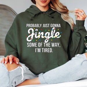 A person wearing a green hoodie with text printed on it, sitting on a bed with their legs crossed.