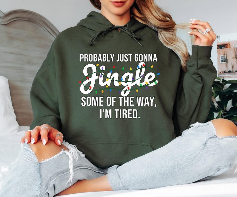 A person wearing a green hoodie with text printed on it, sitting on a bed with their legs crossed.