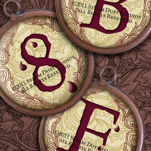 Puede incluir: Tres colgantes circulares con diseños ornamentados y letras rojo oscuro B, 8 y E. Cada colgante tiene un marco marrón y un fondo crema con un estampado floral. El fondo es un diseño floral marrón oscuro.