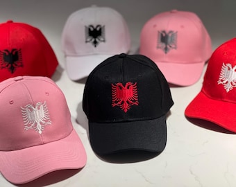 May include: A collection of baseball caps in various colors, including red, pink, white, and black. Each cap features an embroidered emblem of a double-headed eagle. The caps are displayed on a white surface.