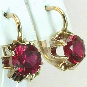 Peut inclure: Une paire de boucles d'oreilles dorées avec de grandes pierres précieuses rouge rubis facettées. Les boucles d'oreilles ont une fermeture à levier et un sertissage décoratif festonné. Les pierres mesurent environ 1,3 cm de diamètre.